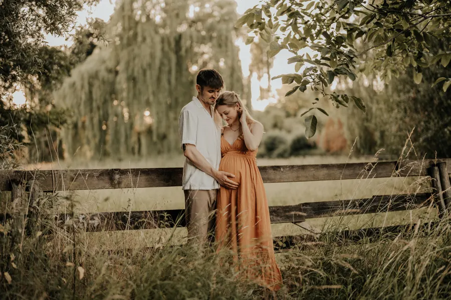 Babybauch-Fotografie, Paar am Holzzaun im Abendlicht